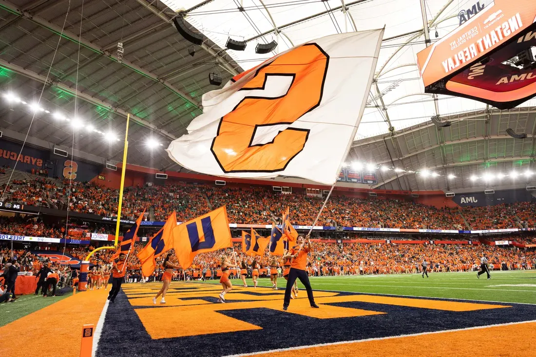 Student running through the JMA Wireless Dome waves flag at Syracuse University football game.